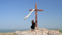 A woman in a black cape kneeling at the Cross.
