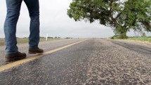feet of a man walking down the center lines of a road 
