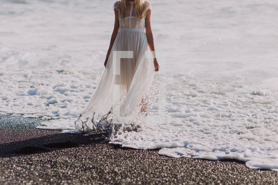 a woman in a flowing sheer dress standing in the tide of the ocean 