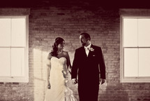 bride and groom holding hands standing in front of a brick wall