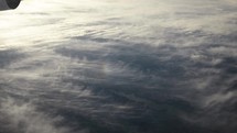 View of earth, sunlight and clouds from airplane window while flying in cinematic slow motion above the clouds in the atmosphere.