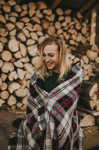 a woman standing in front of a pile of firewood wrapped in a blanket 