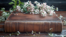 Old Bible on vintage wooden table with some leaves and little white flowers against black wall background