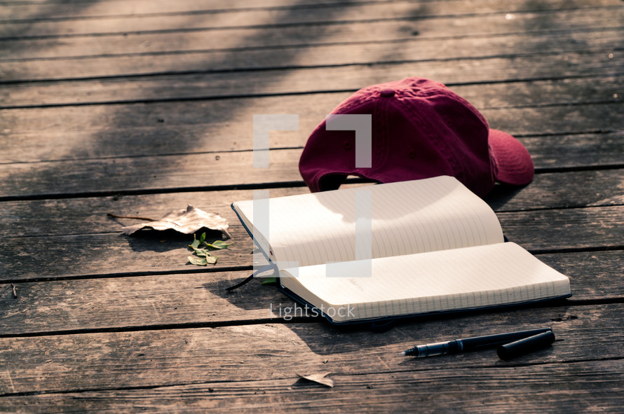 ball cap, open journal, and pen on a wood deck 