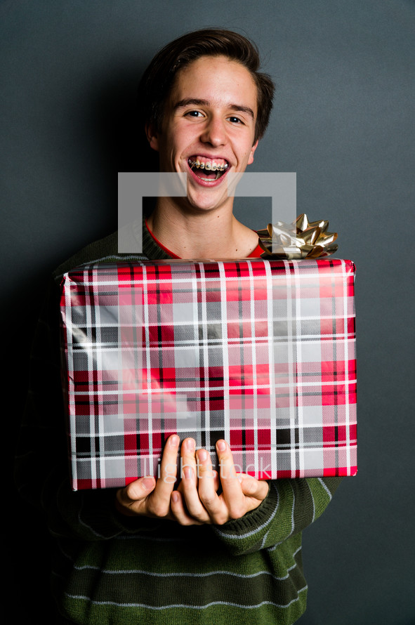 a smiling teen boy with braces holding a Christmas gift 