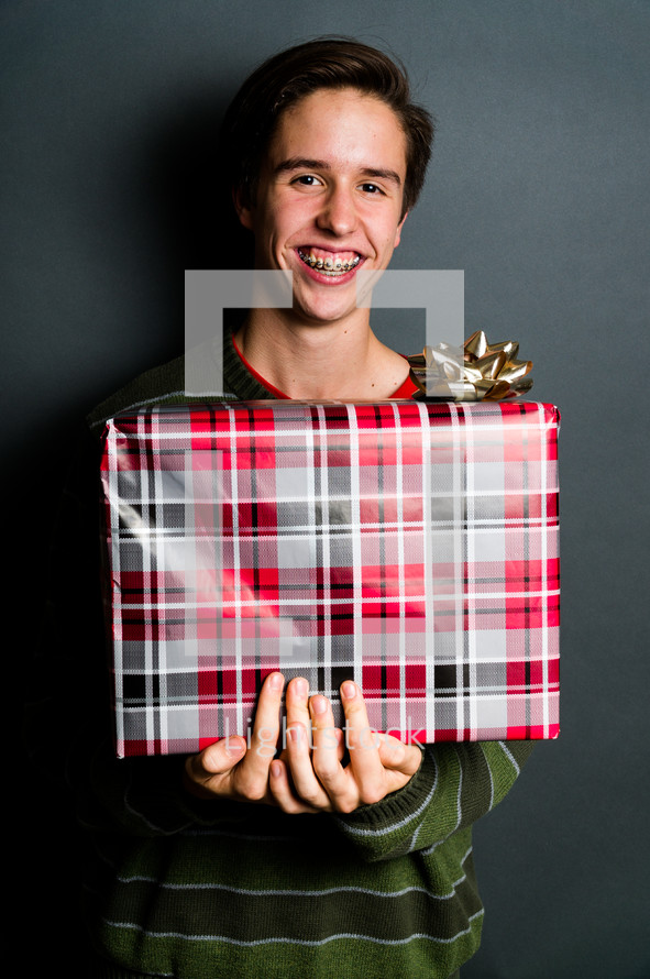 a teen boy with braces holding a wrapped Christmas gift 
