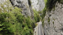 Aerial pullback on cars driving on a narrow road through towering cliffs and lush greenery. Bicaz Gorge in Romania.
