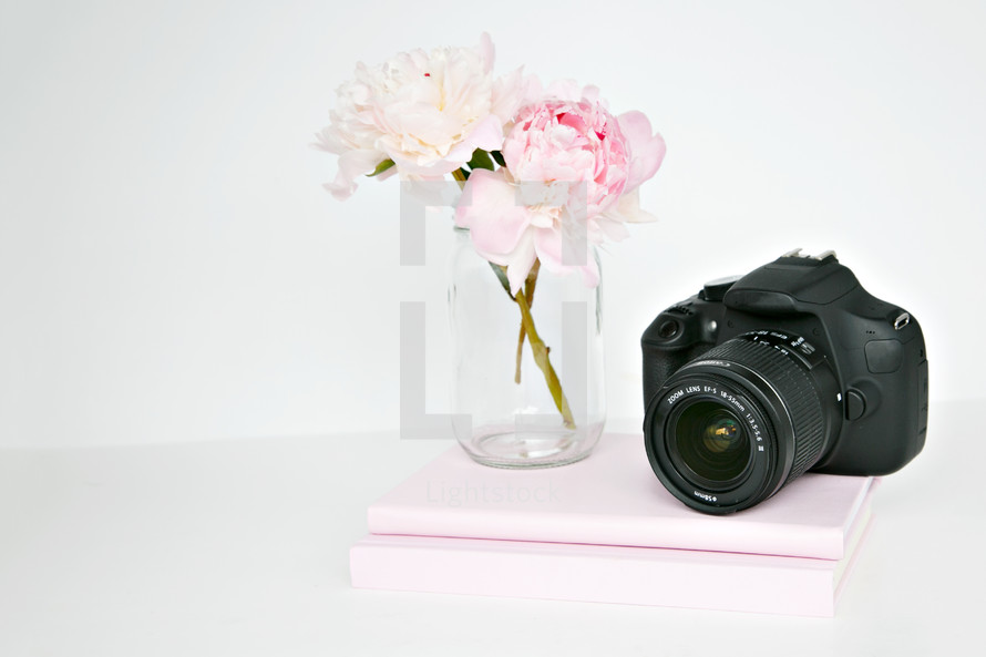 clear vase of flowers and stack of books and camera 