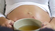 Pregnant woman drinks cup of tea with belly close up 