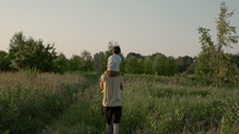 Father walking with son on shoulders in field during summer