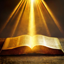 The light of God shines down on the holy bible book laid out open on a wooden table.
