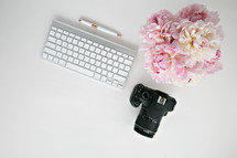 pink flowers, camera, and computer keyboard on a desk 