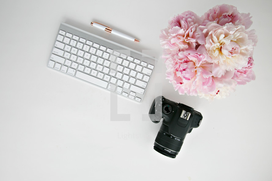 pink flowers, camera, and computer keyboard on a desk 