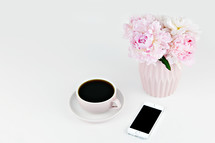 vase of flowers, coffee cup, and cellphone on a white table 