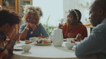 African American family eating sweet cake, drinking tea and having conversation during holiday dinner at home
