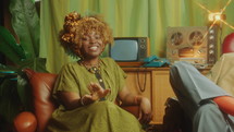 Stylish Black TV host introducing his female colleague smiling and speaking at camera when hosting talk show together in retro-styled studio. Zoom Shot
