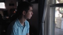 Sad, anxious, depressed, worried young teenage boy looking out a window. 