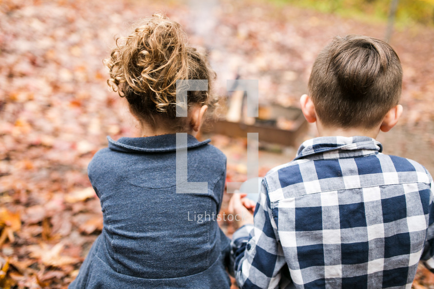 children sitting outdoors with their backs to the camera on a fall day 