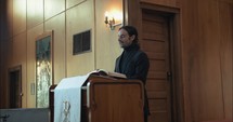 Young pastor in church with bible preaching, teaching sermon to congregation in Sunday morning worship service.