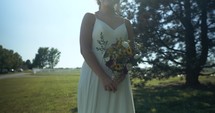 Bride in white dressing with flowers in sunlight on wedding day.