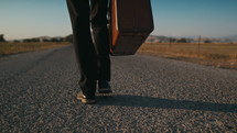 man walking alone on a road carrying a suitcase 