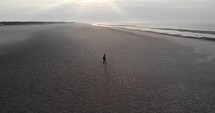 Aerial pan of a man walking on the beach.