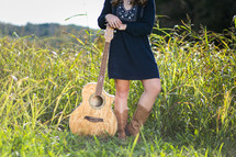 young woman with a guitar standing in a field 