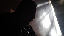 Silhouette of a man sitting and praying with light shining behind him in slow motion.