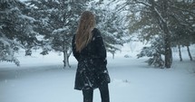 Woman in winter coat walking outside on Christmas, in winter snow as snowflakes fall in cinematic slow motion.