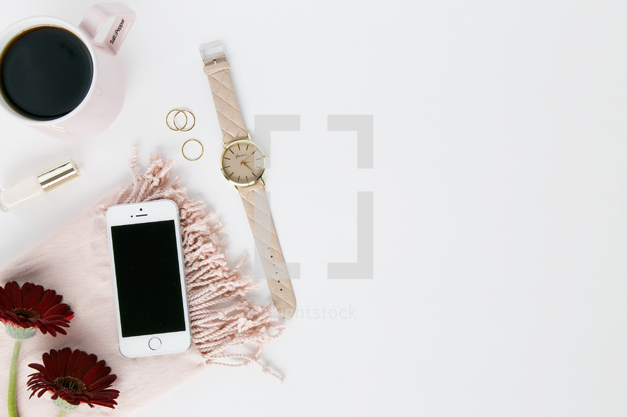 candle, pink scarf, red gerber daisies, watch, nail polish, coffee mug, gold rings, white background, iPhone 