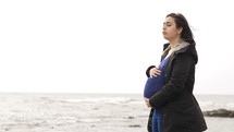 a pregnant young woman standing on a beach 