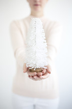 a woman holding a white bottle brush Christmas tree