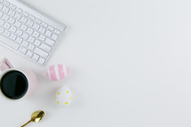 computer keyboard, gold spoon, Easter eggs, and coffee mug on a desk 