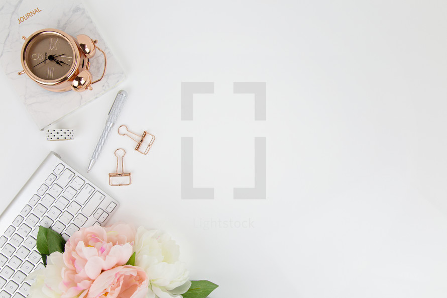 rose gold, alarm clock, flower, computer keyboard, pen, and clips on white desk 