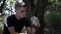 Young man, teenage boy with black eye sitting outside in nature drinking alcohol.