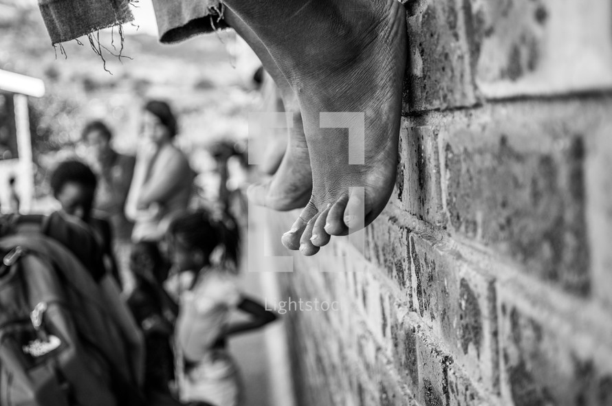bare feet hanging off of a brick wall 