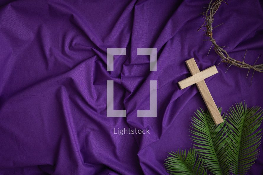 Cross, crown of thorns and palm leaves on a purple cloth background