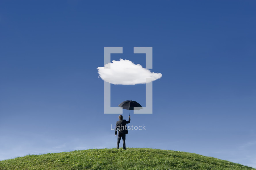 Businessman on a hill holding umbrella underneath a single cloud themes of anticipation protection out of context