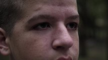 A young, sad man with tears in his eyes. Closeup of face and eyes of a teen boy in nature in cinematic slow motion.