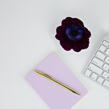 computer keyboard, pen, journal, and flower on a white background 