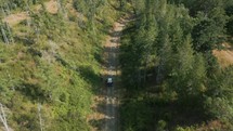 Drone shot following truck down a gravel road on a sunny day.