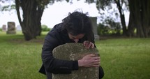 Sad, grieving man embracing family tombstone in cemetery crying in cinematic slow motion. 