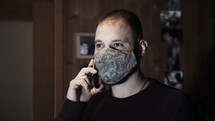 man talking on a cellphone indoors wearing a face mask 