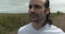 Closeup of face of young man walking on unpaved, dirt road on summer day explore, hiking, worshipping and praying. Lifestyle, worship and prayer concept.