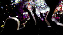 People dancing at live concert with blurry musicians artists and streamers on background