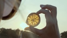 Close-up shot of a woman looking at the sunset through the orange slice