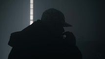 Drug addicted man wearing a hat and hooded coat in a dark, smoky room.