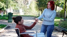 Guy in a wheelchair and girl talking and holding hands.