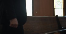 Young, emotional, anxious, and stressed man with long hair and black suit sitting in old church in worship and praying.