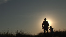 Silhouette of man holding hands with girl and walking towards camera.

